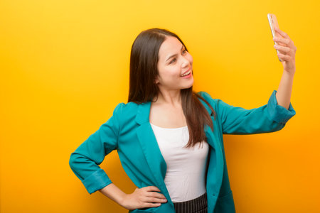 Fashion portrait of beautiful woman in green suit  using cellphone on yellow backgroundの写真素材