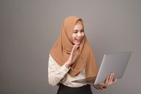 Portrait of beautiful woman with hijab is holding computer laptop on gray background