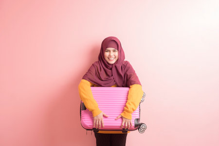 muslim woman with hijab is holding luggage on pink background , people travel concept