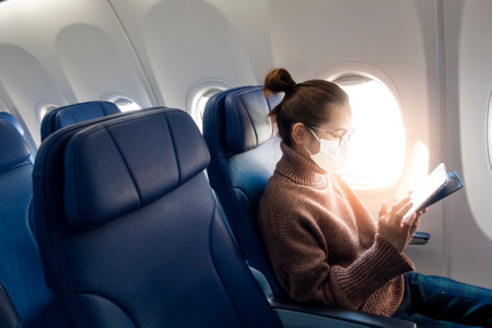 A young woman wearing face mask is traveling on airplane , New normal travel after covid-19 pandemic conceptの写真素材