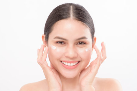 Close up beauty portrait of a young beautiful smiling woman applying face cream over white background studioの写真素材