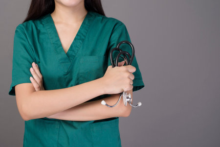 a female doctor wearing a green scrubs and stethoscope is on grey background studioの写真素材