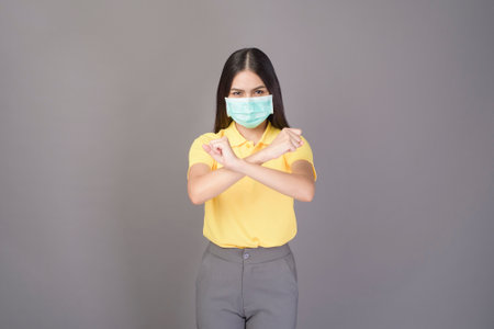 portrait of young confident woman in yellow shirt is wearing surgical mask over grey background...