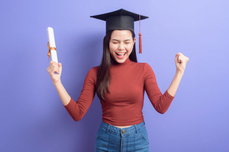 Portrait of young University student woman with graduation cap on violet backgroundの写真素材