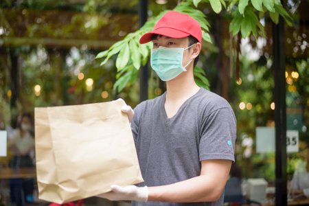An Asian delivery man is wearing face mask, holding grocery bag , Safety home delivery concept