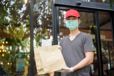An Asian delivery man is wearing face mask, holding grocery bag , Safety home delivery conceptの写真素材