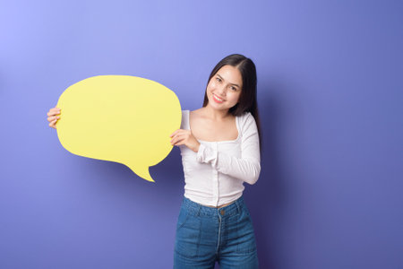 Young woman is holding yellow empty speech on purple backgroundの写真素材