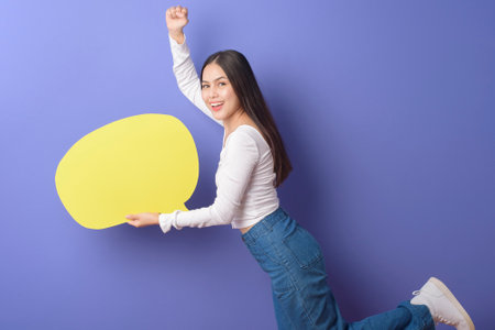 Young woman is holding yellow empty speech on purple background