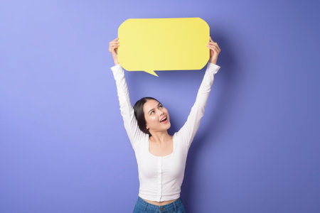 Young woman is holding yellow empty speech on purple background