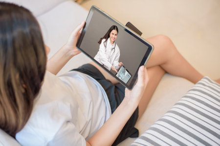 Tablet monitor view over girl shoulder, A doctor woman is wearing  uniform and give consultation to young women about Coronavirus prevention, Health care technology concept.の写真素材