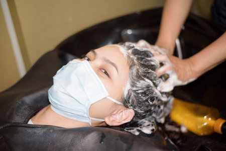 a young woman is getting a haircut in a hair salon , wearing face mask for protectionの写真素材