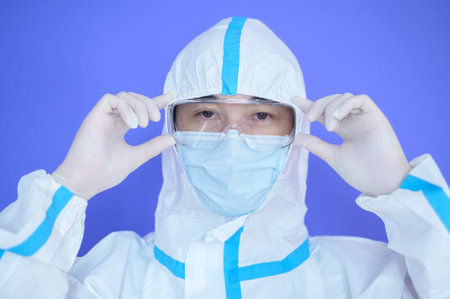 An Asian man is wearing ppe suit on purple background .