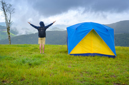 A happy traveling man enjoying and relaxing near camp tent over beautiful green mountain in rainy season, Tropical climate.の写真素材