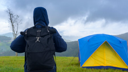 A happy traveling man enjoying and relaxing near camp tent over beautiful green mountain in rainy season, Tropical climate.の写真素材
