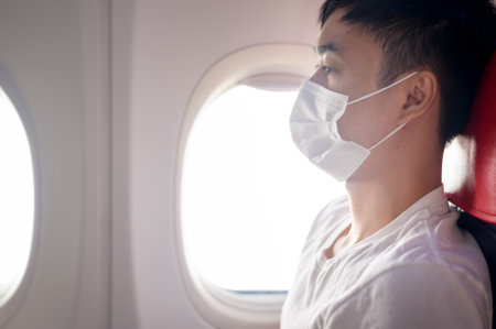 A travelling man is wearing protective mask onboard in the aircraft, travel under Covid-19 pandemic, safety travels, social distancing protocol, New normal travel conceptの写真素材