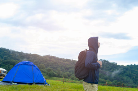A happy traveling man enjoying and relaxing near camp tent over beautiful green mountain in rainy season, Tropical climate.の写真素材