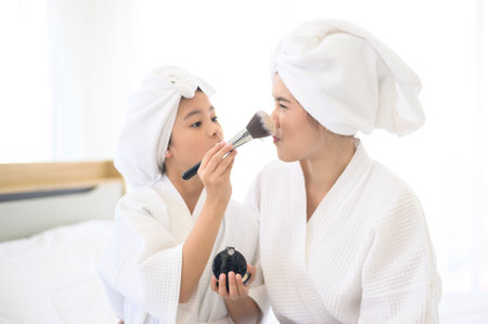 A happy beautiful mom and daughter in white bathrobe applying natural Make-Up with cosmetic powder brush, Family and Beauty Concept.の写真素材