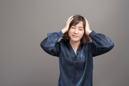 A portrait of young beautiful asian woman is stress and having headache over gray backgroundの写真素材