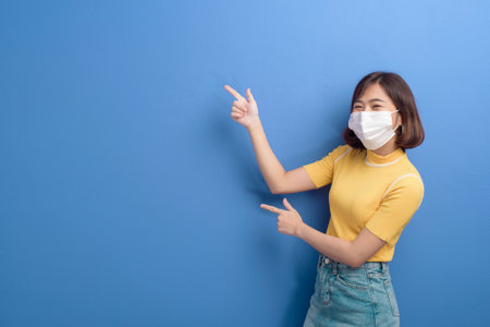A portrait of young beautiful asian woman wearing a surgical mask over studio backgroundの写真素材