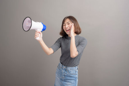 A portrait of young beautiful asian woman holding megaphone over studio background.の写真素材