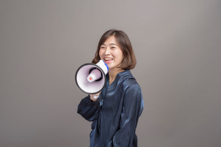 A portrait of young beautiful asian woman holding megaphone over studio background.の写真素材