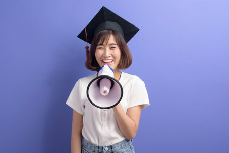 A portrait of graduated asian student holding megaphone isolated purple background studioの写真素材