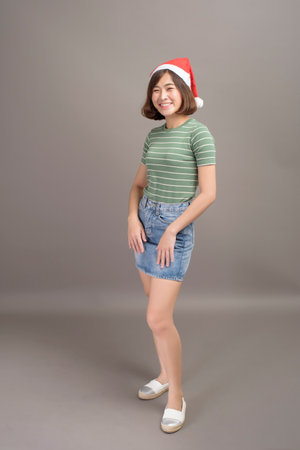 A portrait of beautiful woman wearing red Santa Claus hat holding gift box over studio background, Christmas conceptの写真素材