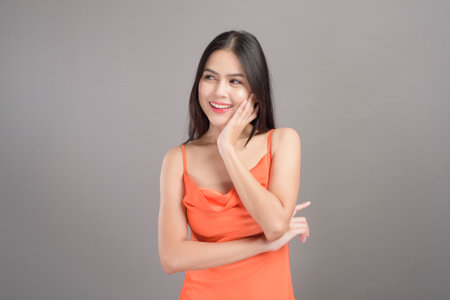 A fashion portrait of beautiful woman wearing orange dress isolated over gray background studioの写真素材