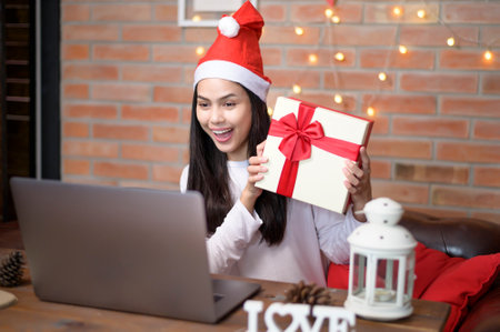 A young smiling woman wearing red Santa Claus hat making video call on social network with family and friends on Christmas day.の写真素材