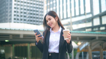 A young business woman wearing black suit is using smart phone , holding a cup of coffee in the city, Business Lifestyle Conceptの写真素材