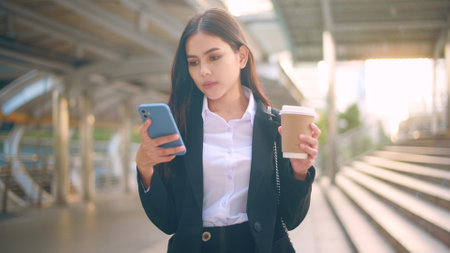 A young business woman wearing black suit is using smart phone , holding a cup of coffee in the city, Business Lifestyle Conceptの写真素材