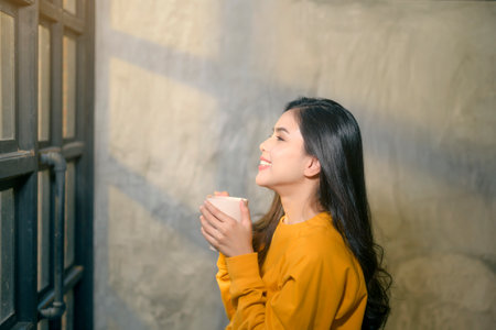A young beautiful woman in sunshine light enjoying her morning coffee at home.の写真素材