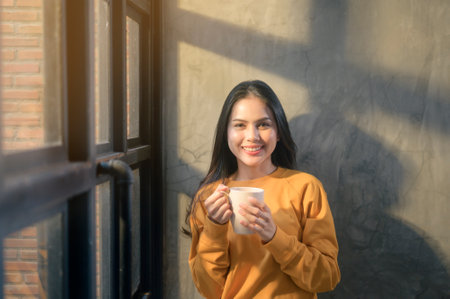 A young beautiful woman in sunshine light enjoying her morning coffee at home.の写真素材