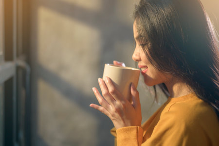 A young beautiful woman in sunshine light enjoying her morning coffee at home.の写真素材