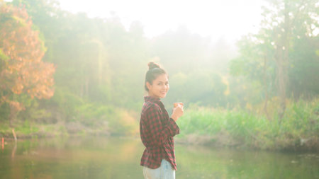 A beautiful young traveler woman is enjoying with nature drinking coffee in the morning over lake, relaxation , camping holiday and travel concept .の写真素材