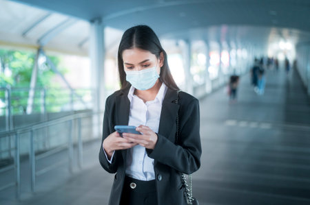 Young business woman with face mask  is standing on metro platform using smart.の写真素材