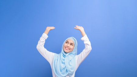 Portrait of a young muslim woman with hijab over blue background studio.の写真素材