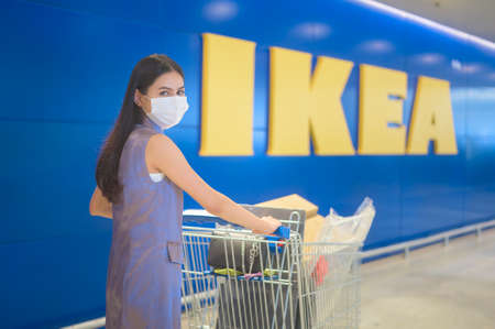 A young woman wearing a surgical mask with a shopping trolley at ikeal, covid-19 and pandemic concept.のeditorial素材