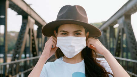 close up beautiful woman is wearing surgical mask on the Bridge, safety travel concept.の写真素材