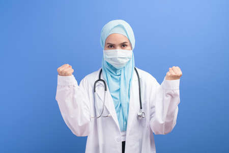A female muslim doctor with hijab wearing a surgical mask over blue background studio.の写真素材