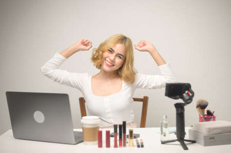 A young blonde woman entrepreneur working with laptop presents cosmetic products during online live...