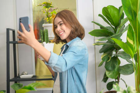 A happy young woman taking selfie with her plants and making video call at home