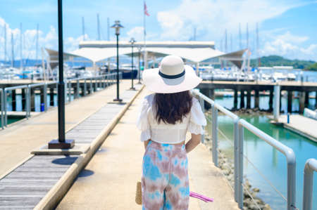 An excited tourist in white hat enjoying and standing on the dock with luxury yachts during summerの写真素材