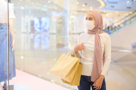 A young muslim woman wearing protective mask in shopping mall, shopping under  pandemic concept.の写真素材