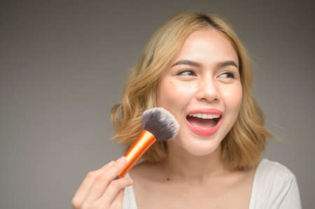 A portrait of young blonde woman holding cosmetic products over white background studio, beauty and make up conceptの写真素材