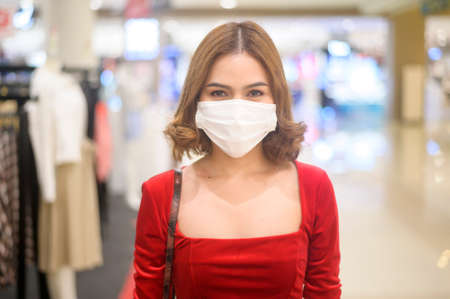 A young woman in red dress wearing protective mask in shopping mall, shopping under  pandemic concept.の写真素材