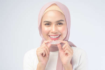 A young muslim woman holding invisalign braces over white background studio, dental healthcare and...