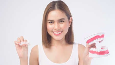 A young smiling woman holding invisalign braces and artificial Dental Model over white background...