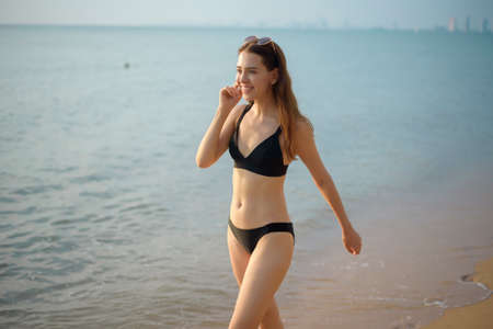 Beautiful woman in black bikini is walking on the beachの写真素材