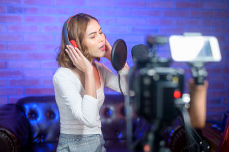 A young smiling female singer wearing headphones with a microphone while recording song in a music...